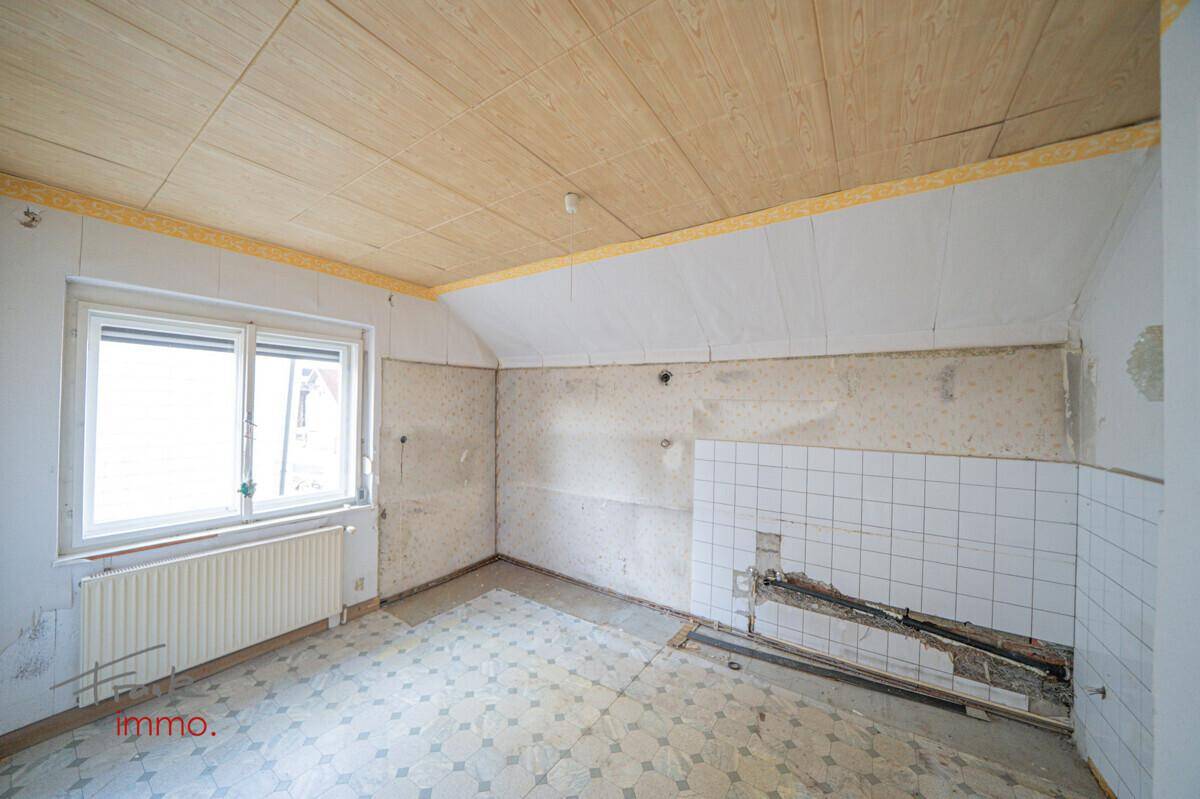 Renovierungsbedürftige Küche im Dachgeschoss mit schräger Decke und alten Fliesen, bietet viel Potenzial.