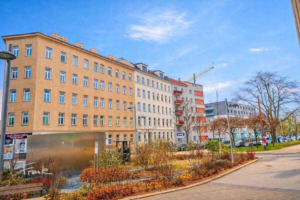 Ansicht einer städtischen Straße mit Gebäuden unterschiedlicher Architektur und einer Grünanlage.