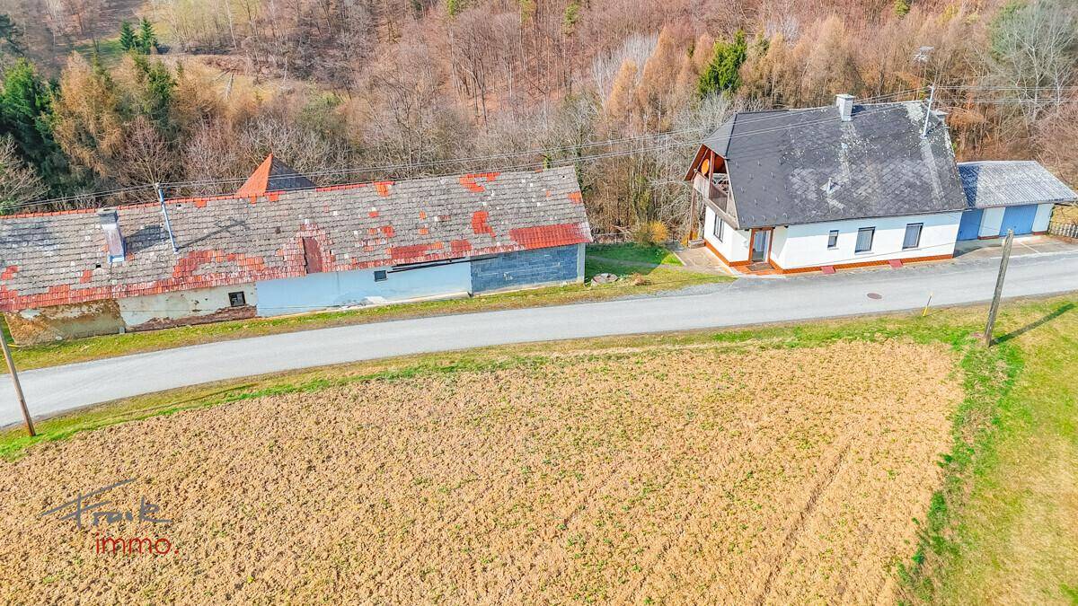Weitläufige Ansicht eines ländlichen Grundstücks mit Wohnhaus, Scheune und Feldern in hügeliger Umgebung.