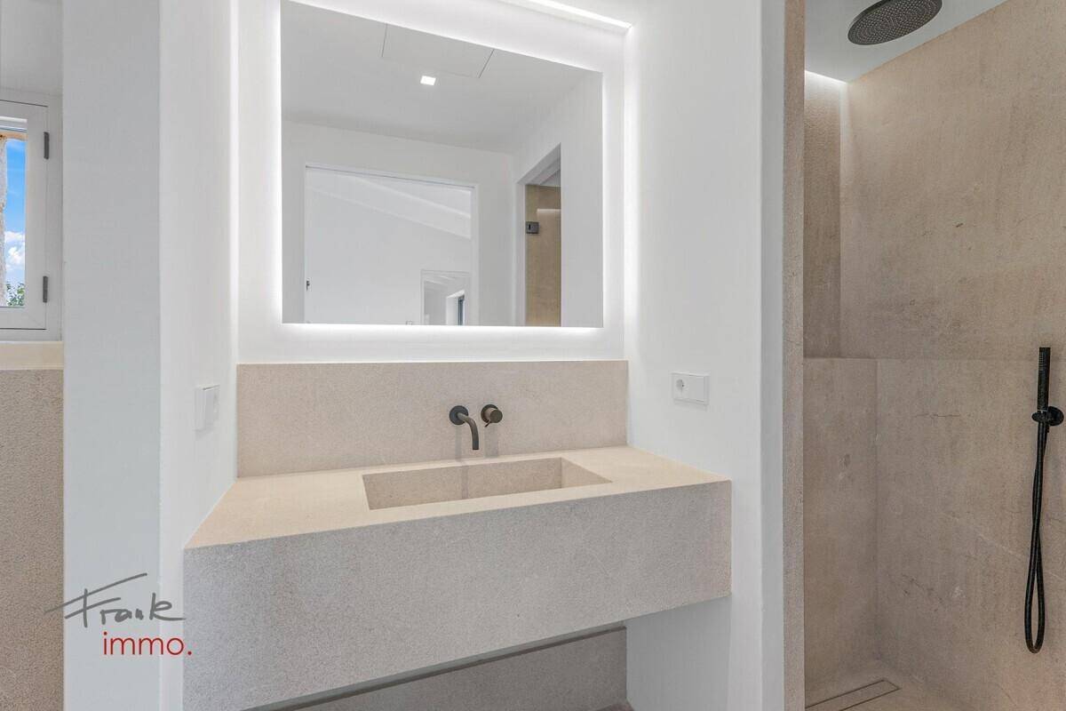 Elegantes Badezimmer mit modernem Waschtisch, beleuchtetem Spiegel und geräumiger begehbarer Dusche.