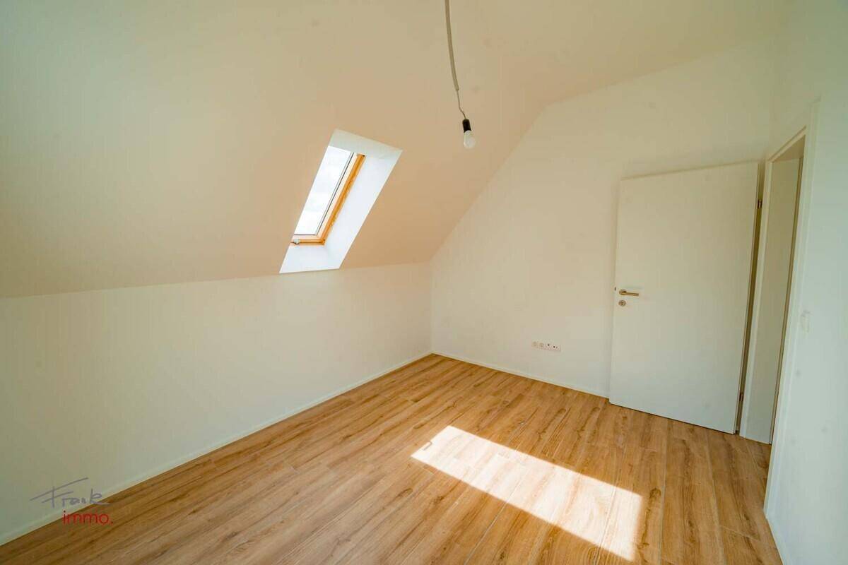 Zimmer mit Dachschräge, Holzoptik-Fliesenboden und einem Dachfenster für Tageslicht.