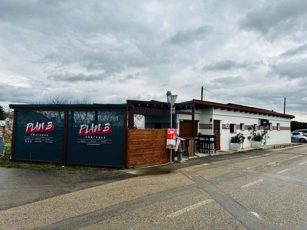 Außenansicht eines modernen Imbissgebäudes mit Holzverkleidung und Parkplätzen unter bewölktem Himmel.