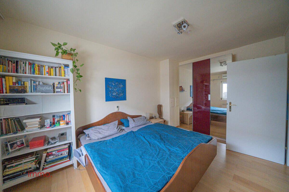 Schlafzimmer mit Holzbett, Bücherregal und großem Spiegelschrank, der den Raum erweitert.