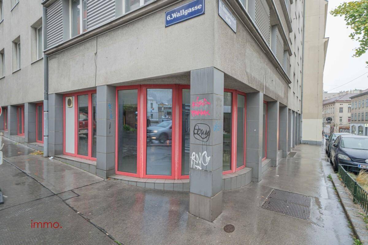 Eckansicht des Gebäudes mit großen Schaufenstern und roten Rahmen an einer belebten Straße.