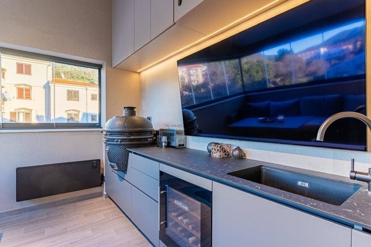 Funktionale Außenküche mit Grill, Spüle und Weinkühler, mit Blick aus dem Fenster.
