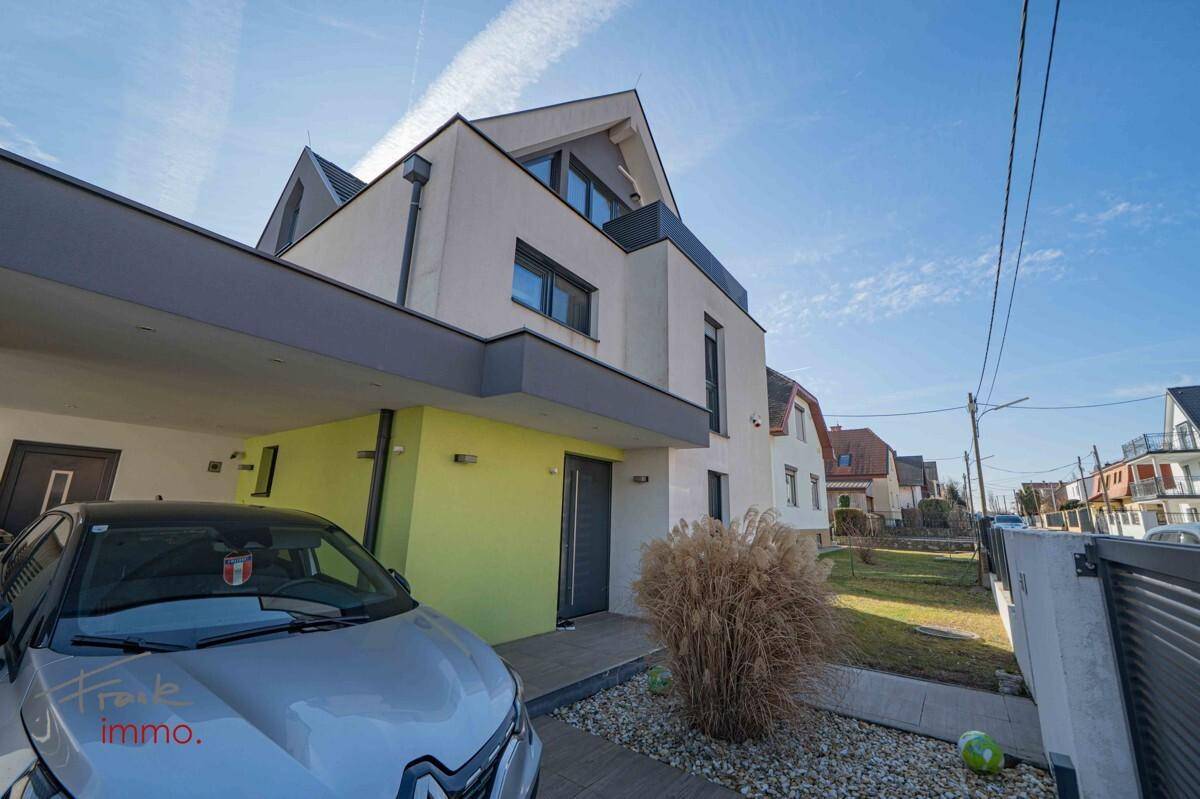 Moderne Hausfassade mit Carport und Vorgarten unter blauem Himmel.
