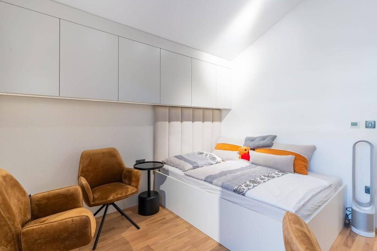 Modernes Schlafzimmer mit Einzelbett, zwei Sesseln und integrierten Oberschränken.