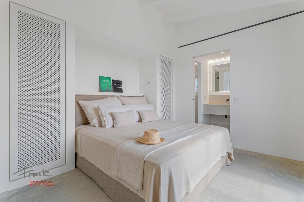 Modernes Schlafzimmer mit hellem Bett, minimalistischer Einrichtung und Zugang zum Badezimmer.