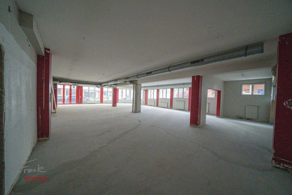 Heller Gewerberaum mit roten Säulen, Betonboden und Fenstern, die Tageslicht hereinlassen.