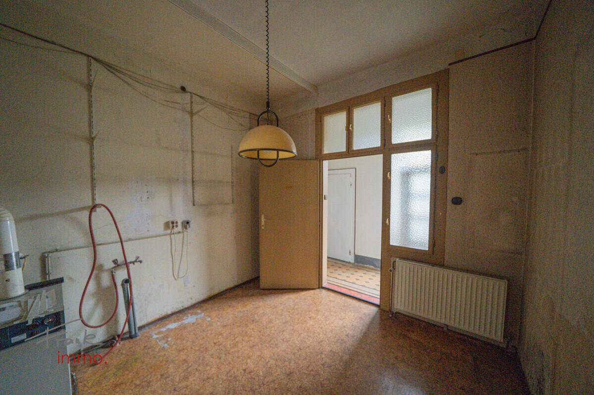 Raum in ursprünglichem Zustand mit Linoleumboden, Heizkörper und einer Tür mit Glasoberlicht.