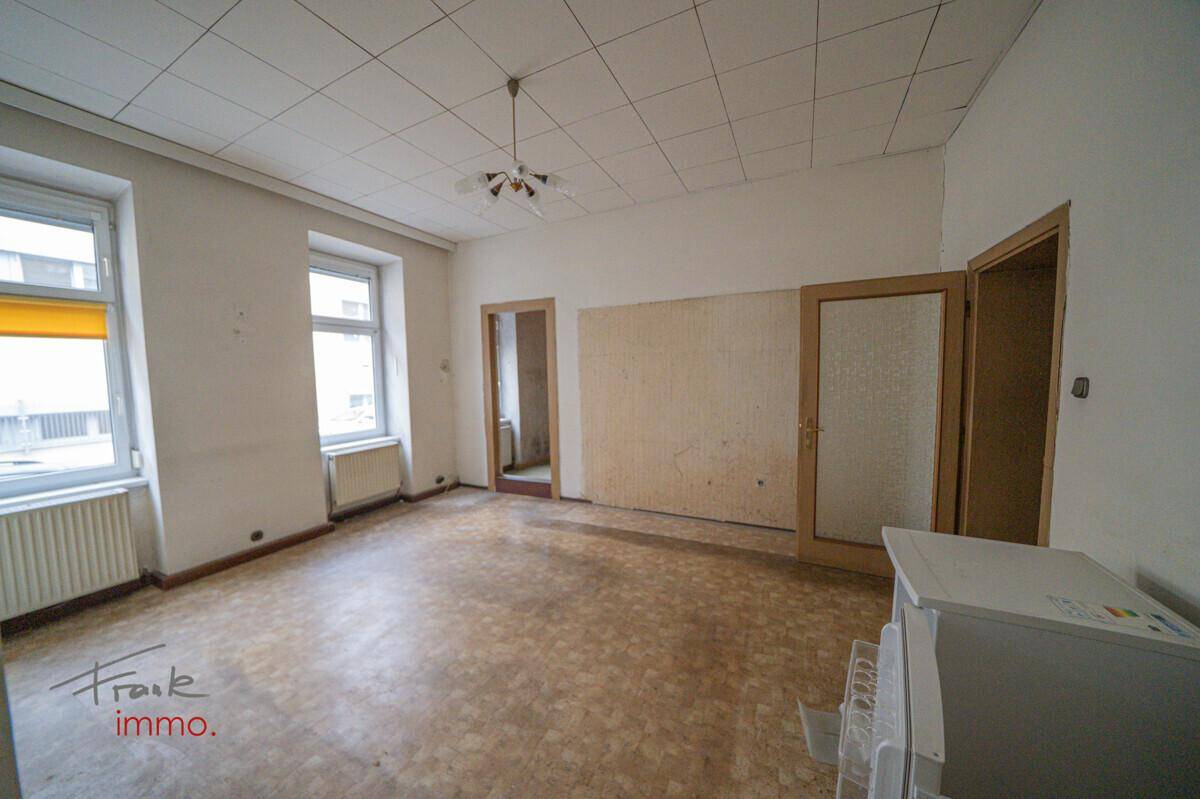 Geräumiger Wohnraum mit Linoleumboden, Kassettendecke und zwei Fenstern.