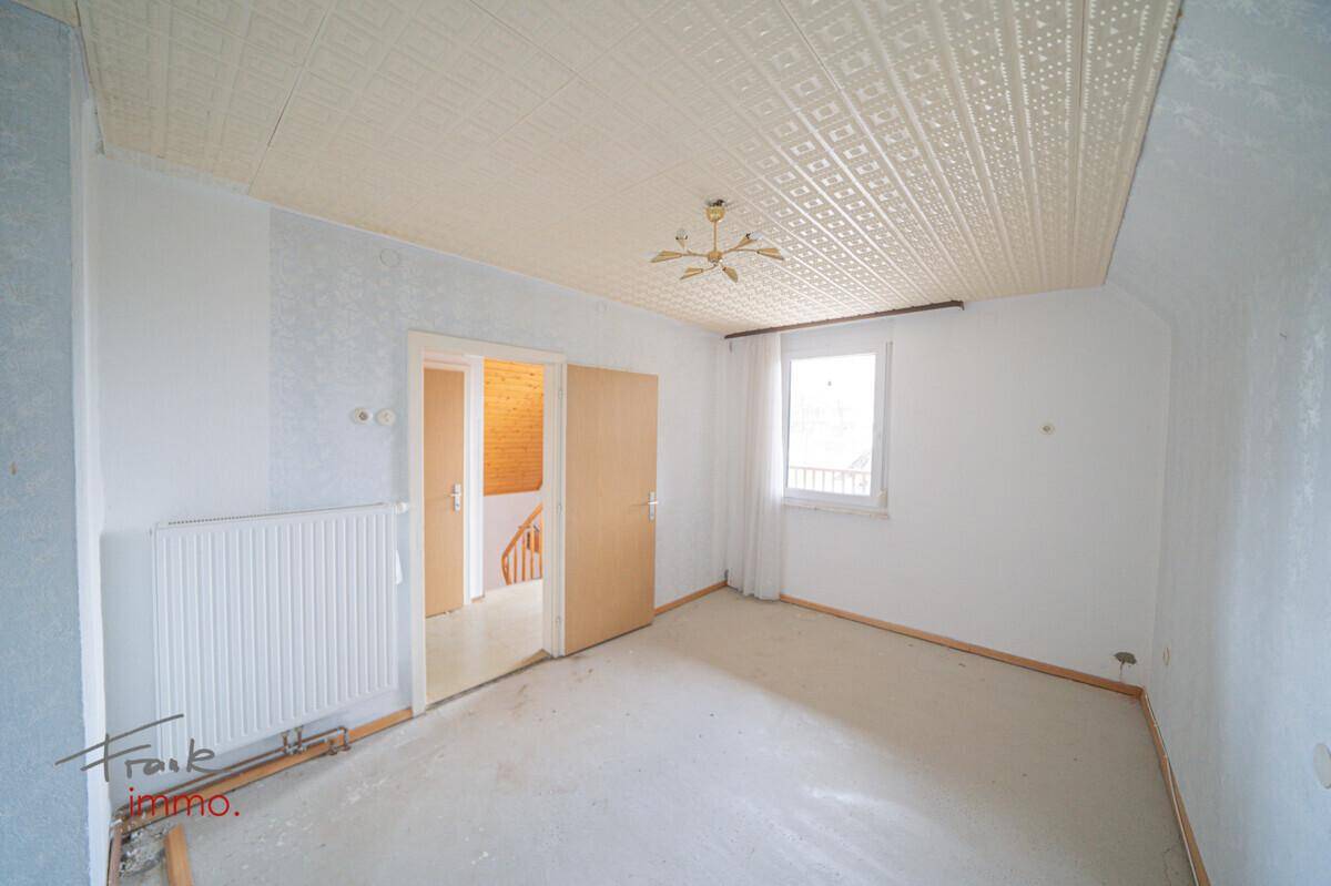 Helles Zimmer mit Teppichboden, Fenster und Zugang zum Flur, in gutem Zustand.