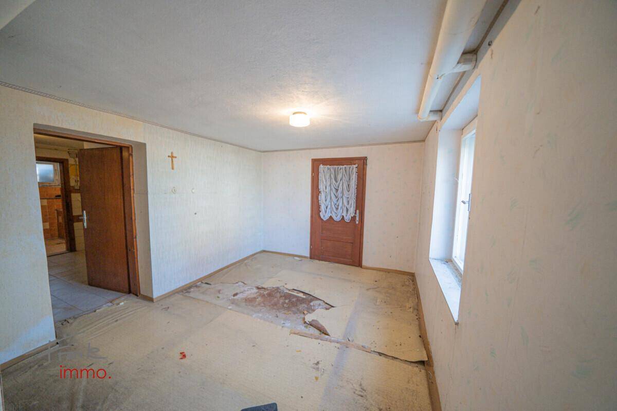 Renovierungsbedürftiger Raum mit beschädigtem Bodenbelag, Tapetenresten und einem Fenster für Tageslicht.