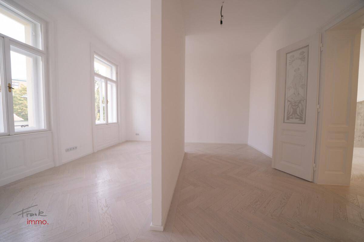 Heller Innenraum mit Fischgrätparkett und hohen Fenstern, der verschiedene Bereiche des Apartments verbindet.