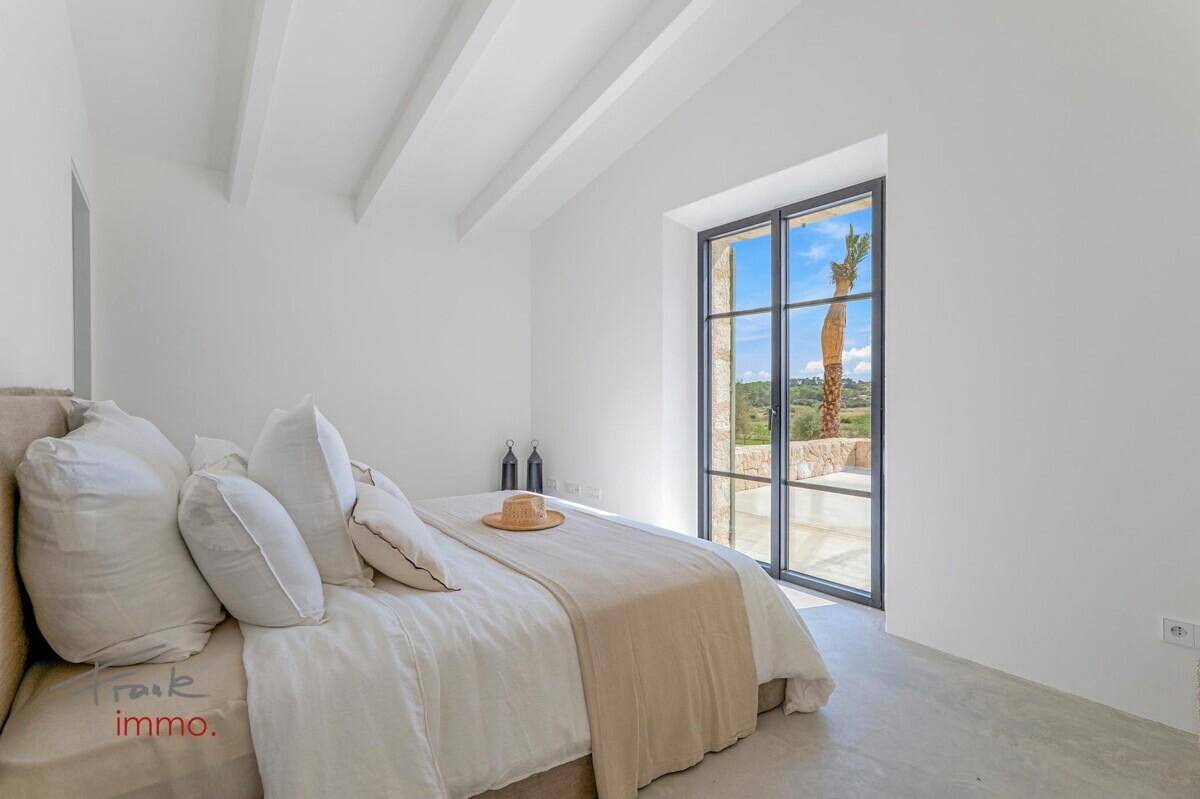 Helles Schlafzimmer mit hoher Decke, sichtbaren Balken und großem Fenster mit Blick auf Palmen.