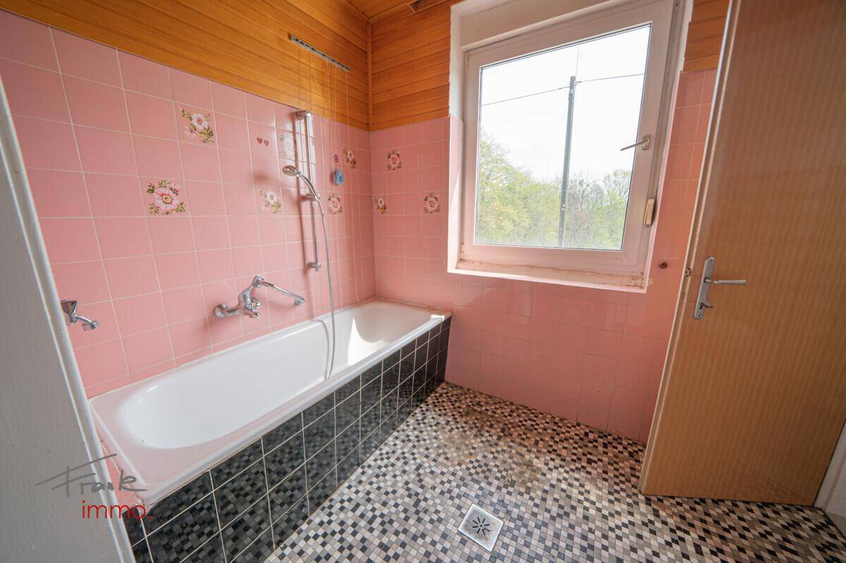 Badezimmer im Stil der 80er Jahre mit rosa Wandfliesen, Badewanne und Fenster.