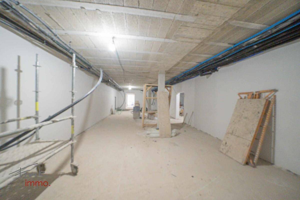 Langer Kellerraum im Rohbau mit sichtbaren Leitungen und Baugerüst.