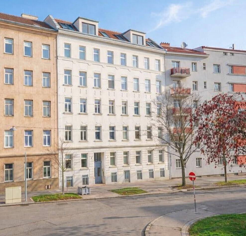 Klassisches Mehrfamilienhaus mit weißer Fassade und vielen Fenstern an einer städtischen Straße.