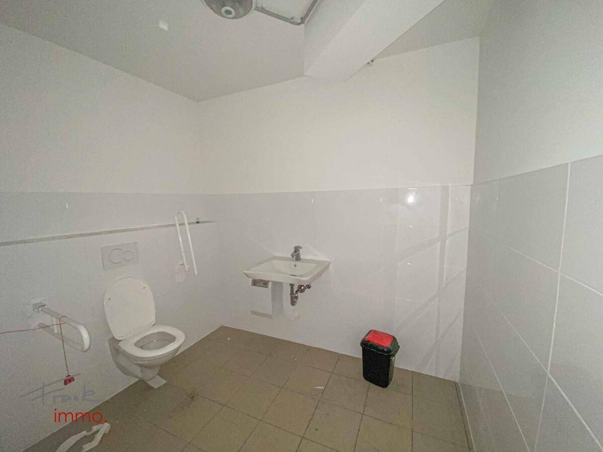 Barrierefreie Toilette mit Haltegriffen, Waschbecken und Fliesen an Wänden und Boden.