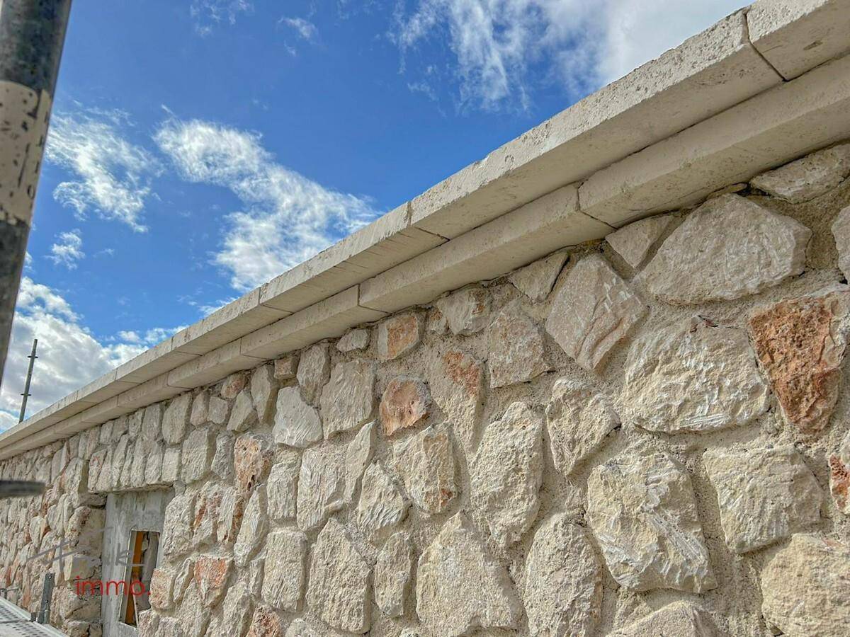 Außenmauer eines Gebäudes aus Naturstein unter blauem Himmel.