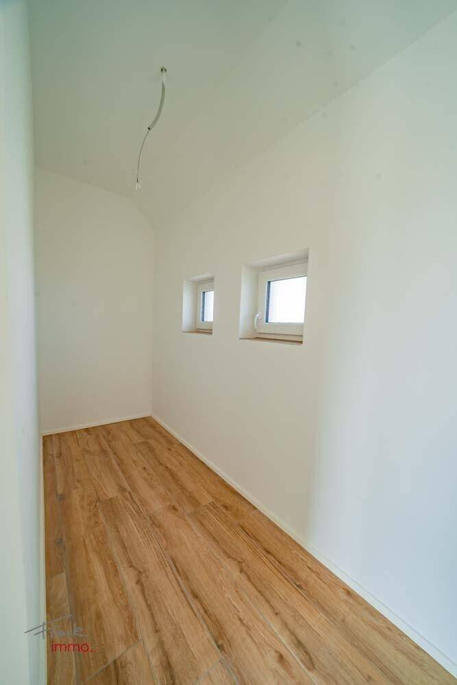 Kleiner Raum mit Holzoptik-Fliesenboden und zwei Fenstern, ideal als Abstellraum oder Büro.