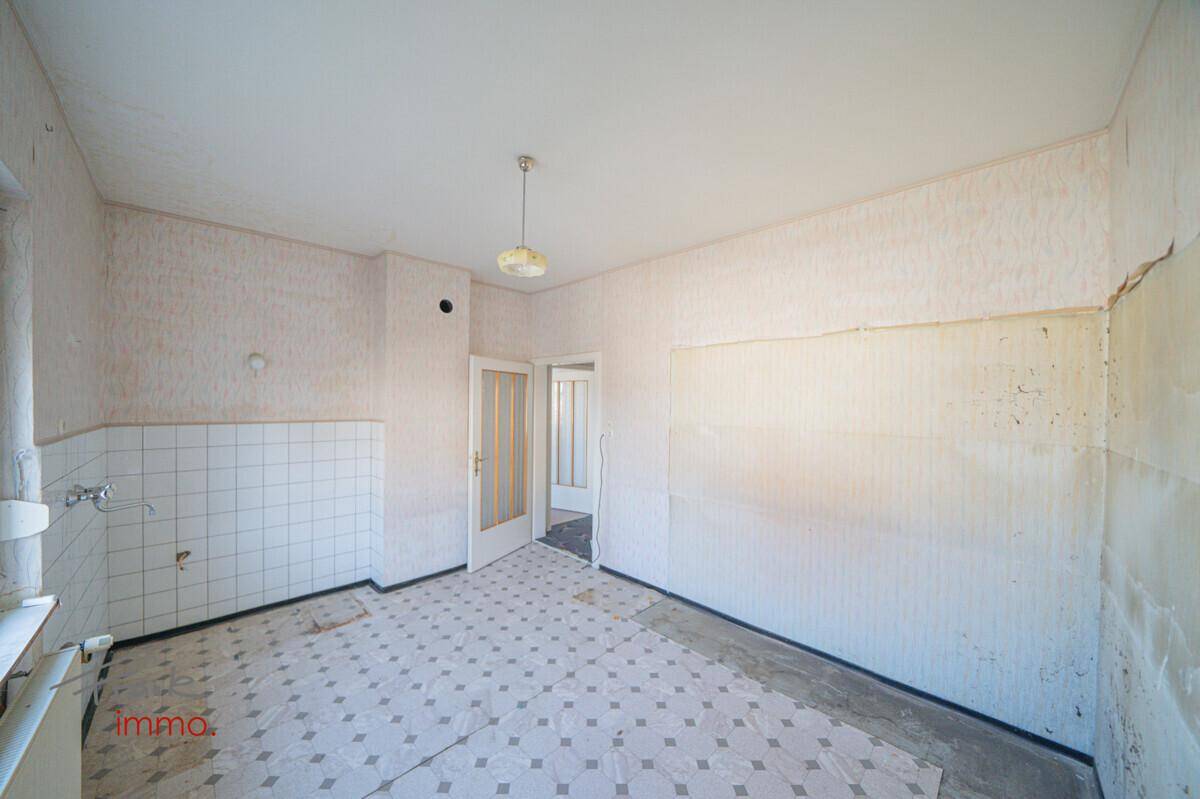 Leere Küche mit alten gemusterten Bodenfliesen und Wandfliesen, wartet auf eine Modernisierung.