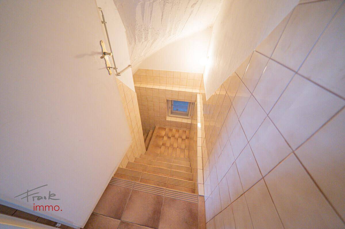 Gefliestes Treppenhaus mit Tageslicht durch ein Dachfenster, das nach oben führt.