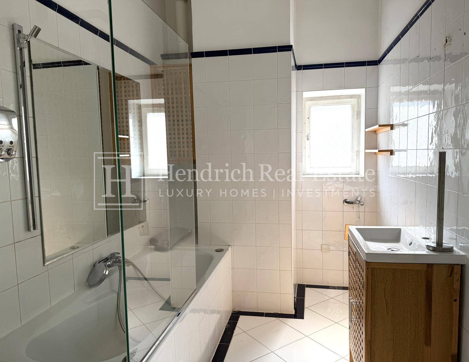 Gefliestes Badezimmer mit Badewanne, Waschbecken und einem Fenster für natürliche Belüftung.