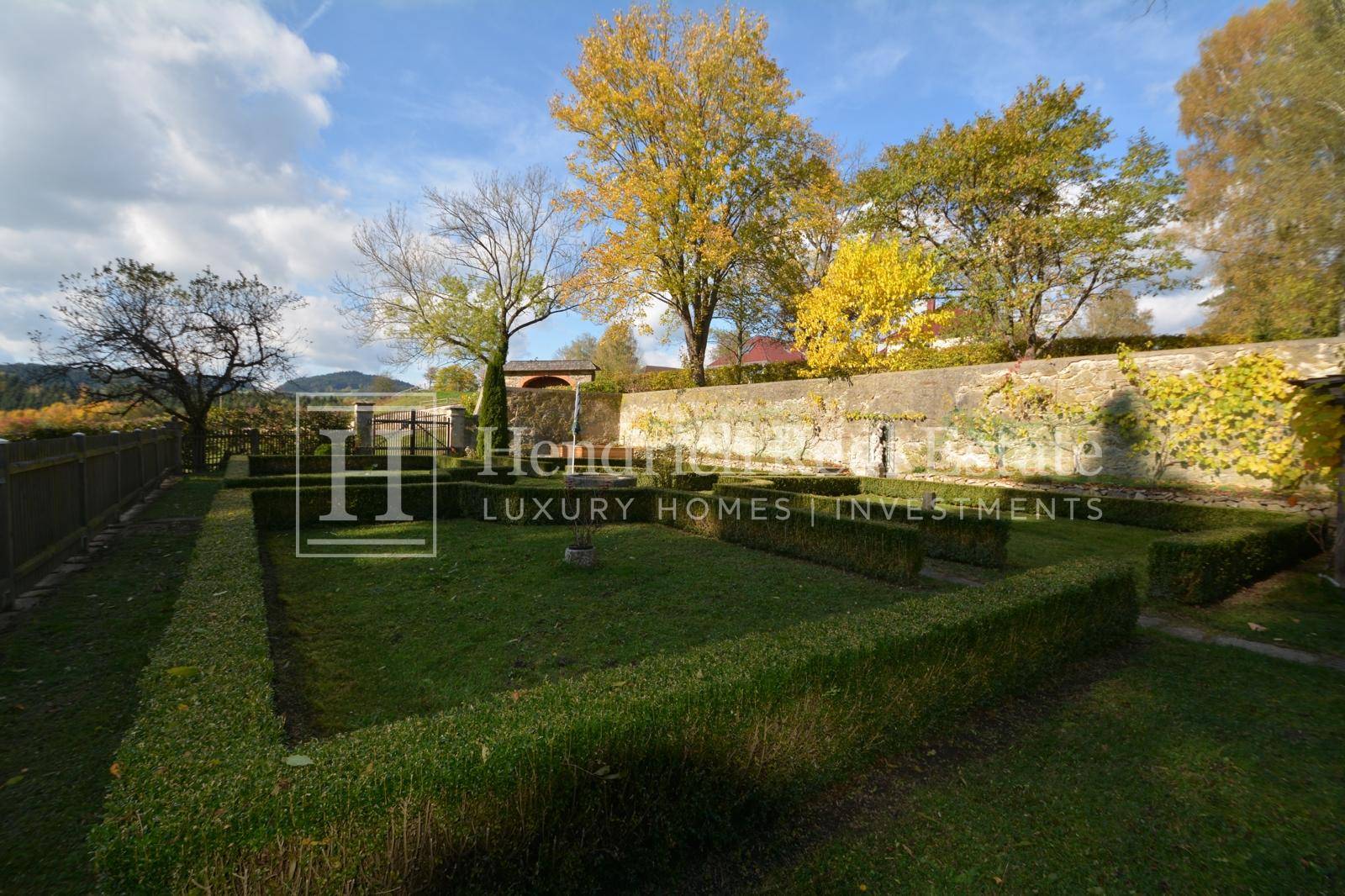 Gepflegter formaler Garten mit geometrisch geschnittenen Hecken, Rasenflächen und altem Baumbestand.