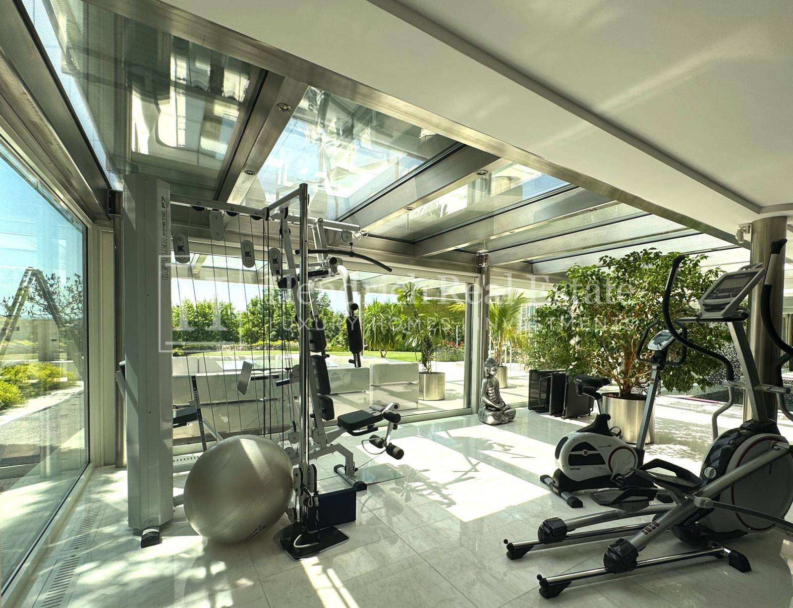 Heller Fitnessraum mit verschiedenen Trainingsgeräten und großen Glasflächen für viel Tageslicht.