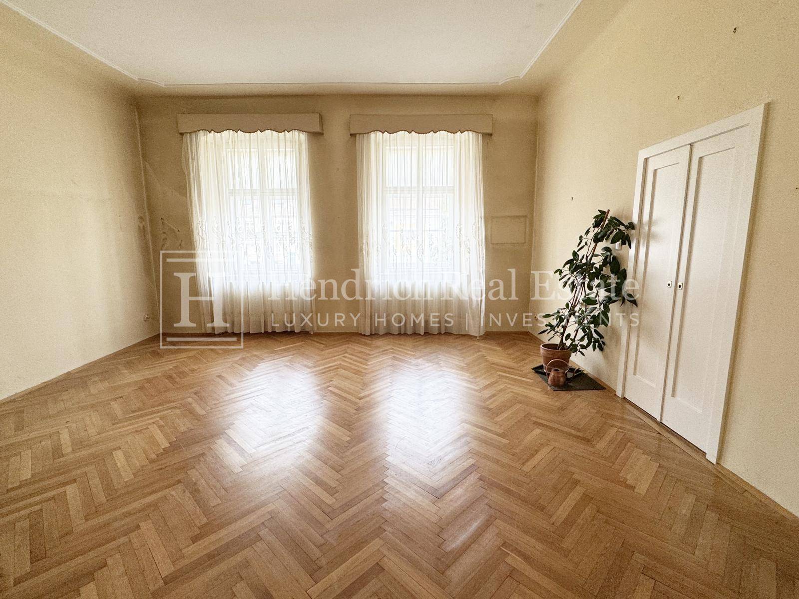 Helles Wohnzimmer mit zwei großen Fenstern, Fischgrätparkett und hohen Decken.