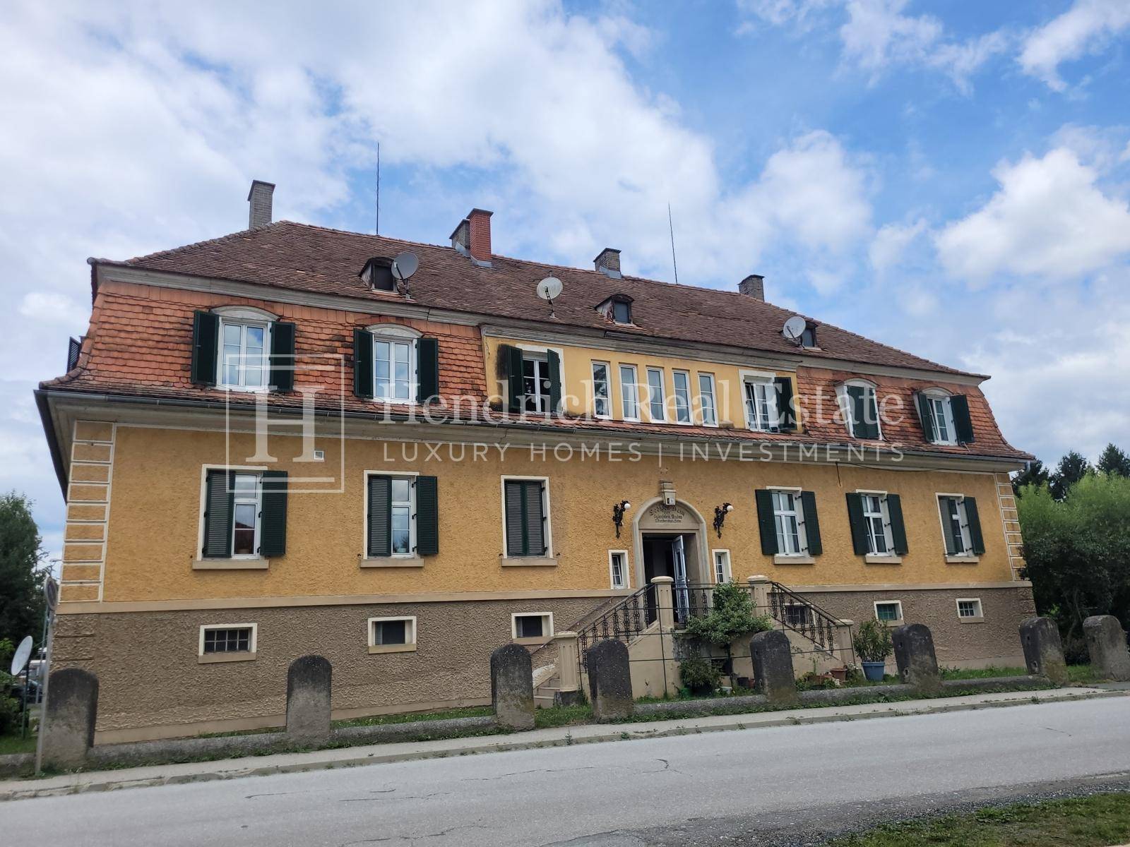 Eindrucksvolles historisches Gebäude mit gelber Fassade, Mansarddach und repräsentativem Eingangsbereich.