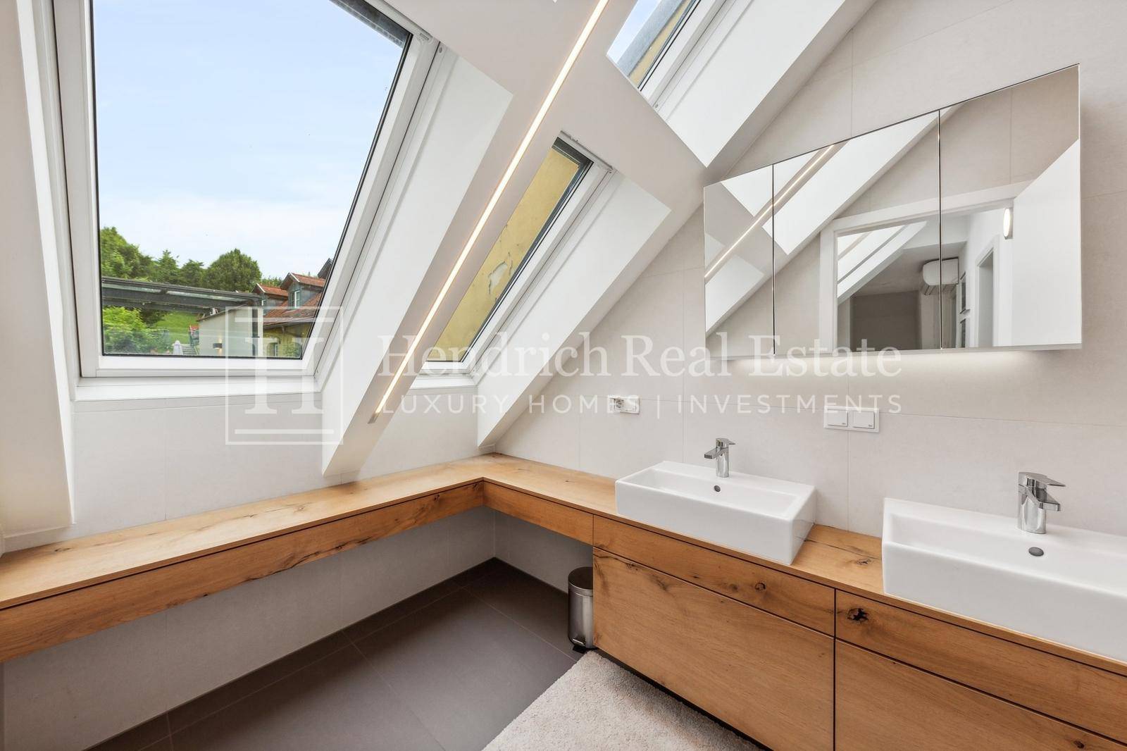 Modernes Badezimmer mit Doppelwaschbecken, Holzunterschrank und mehreren Dachfenstern.