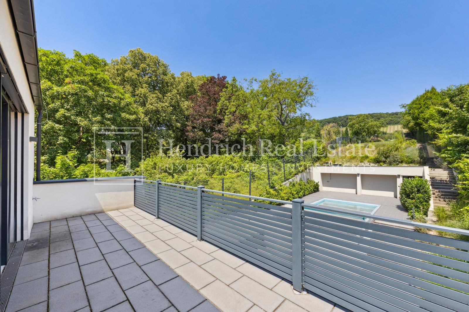 Große gepflasterte Terrasse mit moderner Brüstung und weitem Blick ins Grüne.
