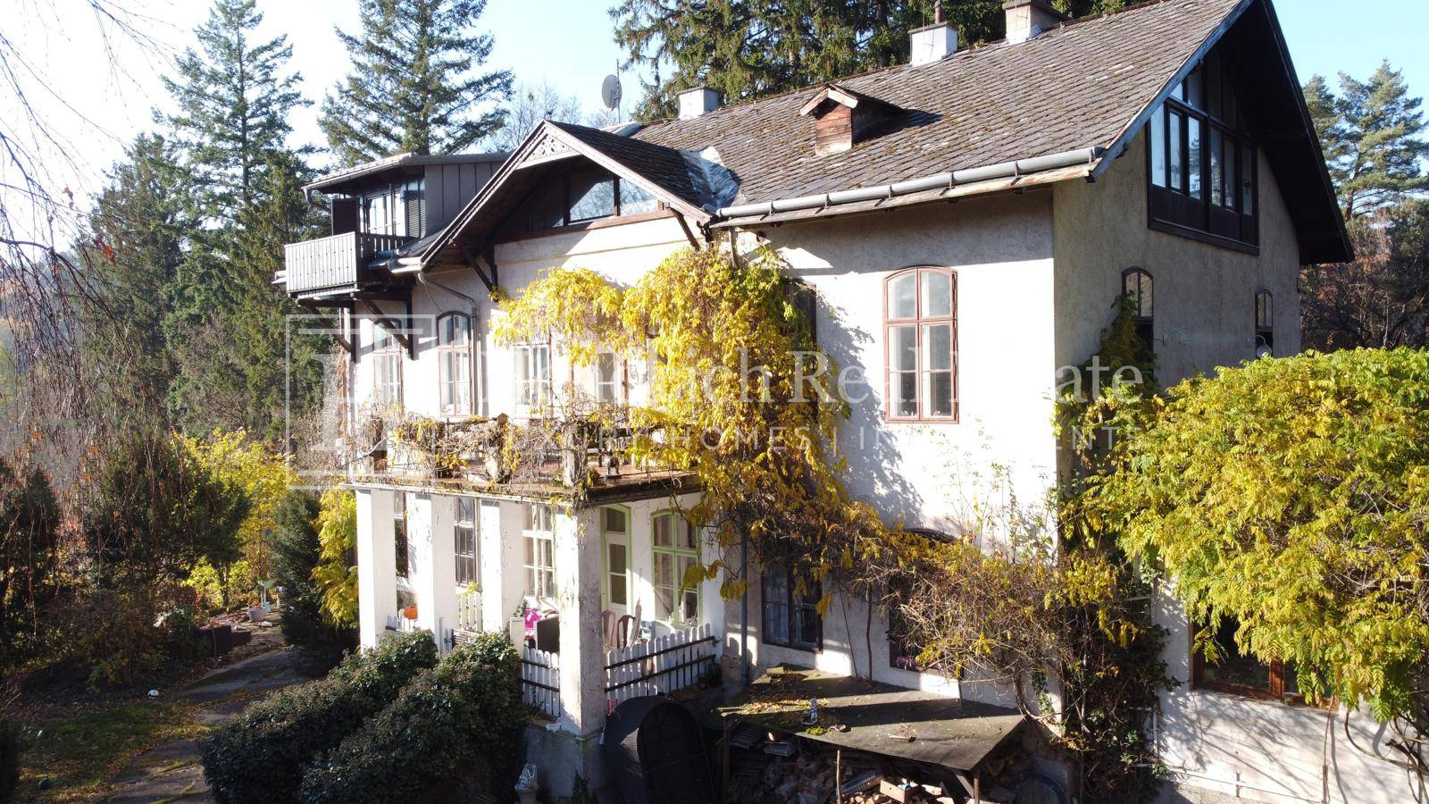 Seitenansicht des Hauses mit mehreren Balkonen, bewachsenen Fassaden und umgebenden Bäumen.