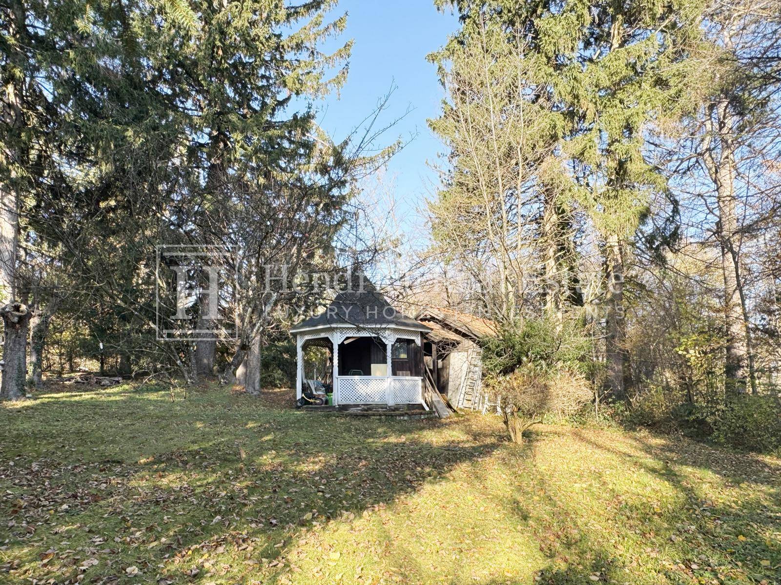 Großer Gartenbereich mit einem charmanten weißen Pavillon, umgeben von hohen Bäumen.