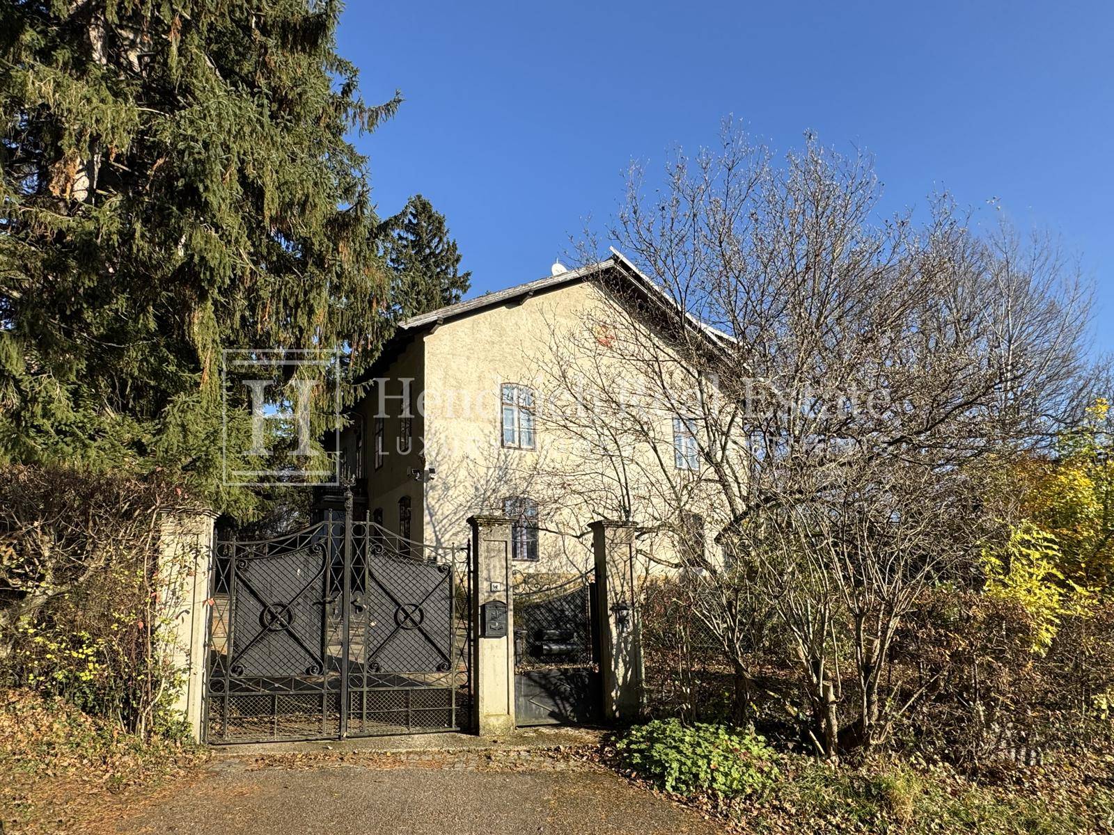 Ansicht des Hauses von der Straße mit einem großen schmiedeeisernen Tor und alter Bausubstanz.