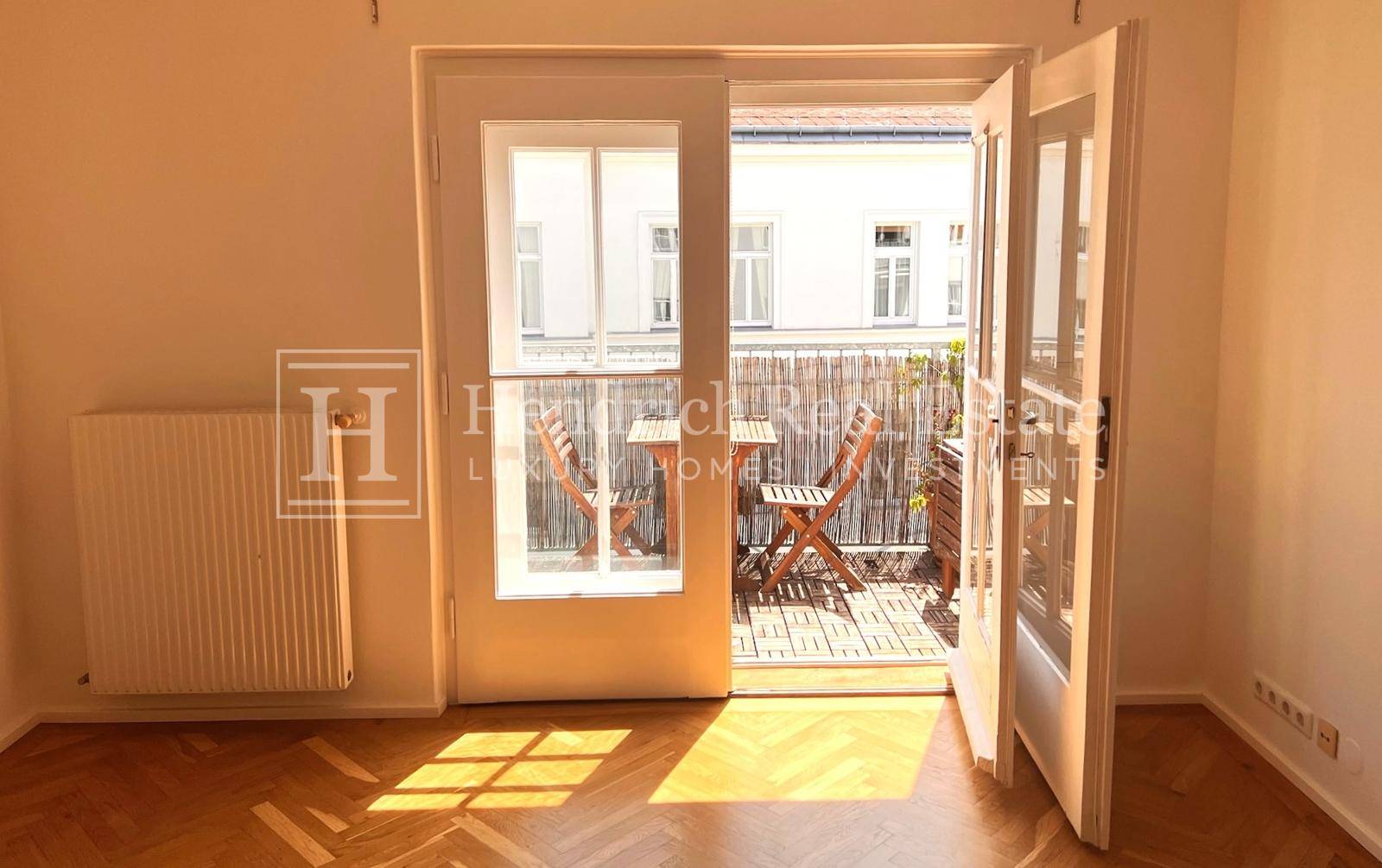 Heller Raum mit Fischgrätparkett und direktem Zugang zu einem sonnigen Balkon.