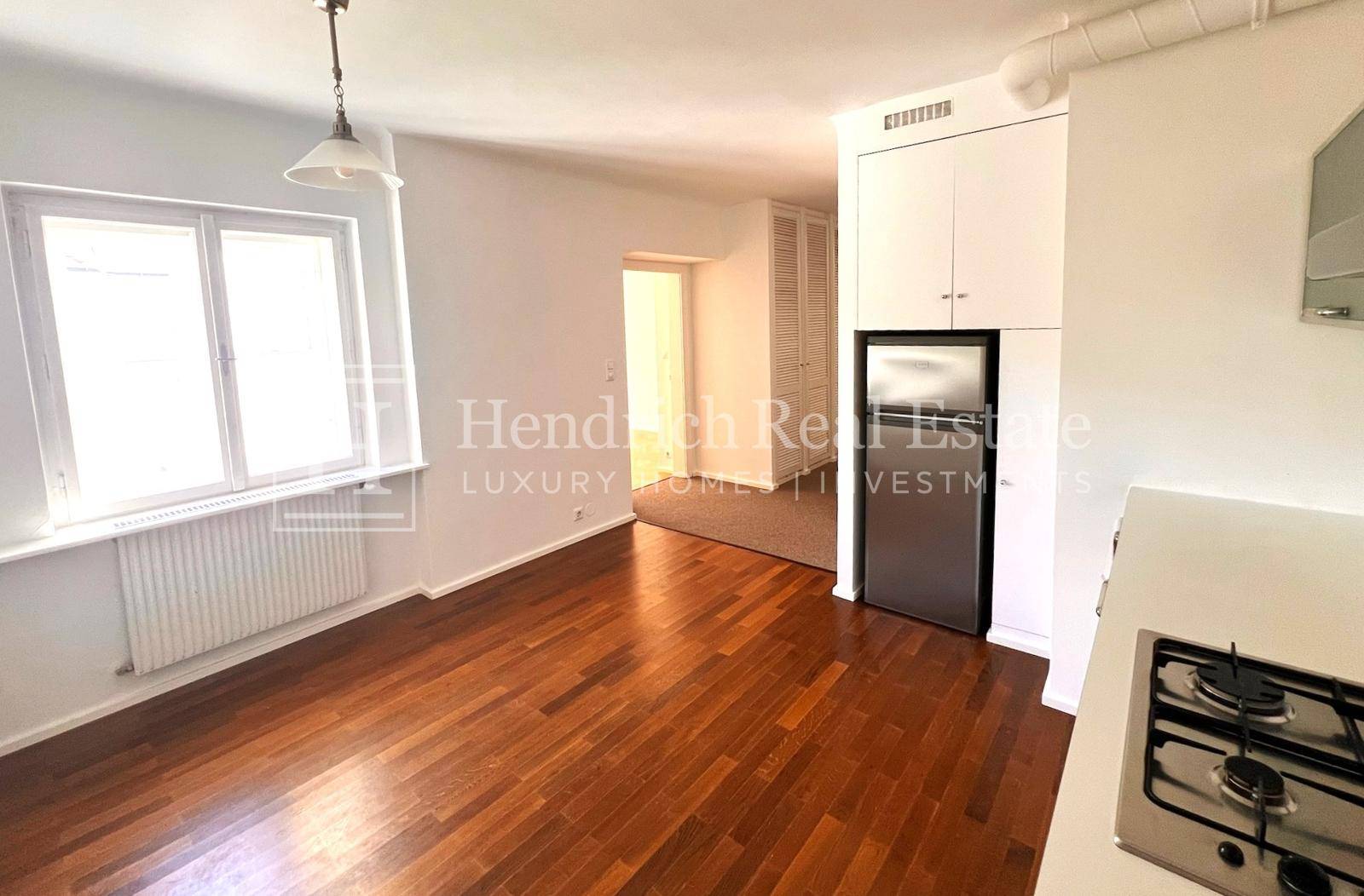 Helle Küchenzeile mit Fenster, Kühlschrank und ausreichend Stauraum.