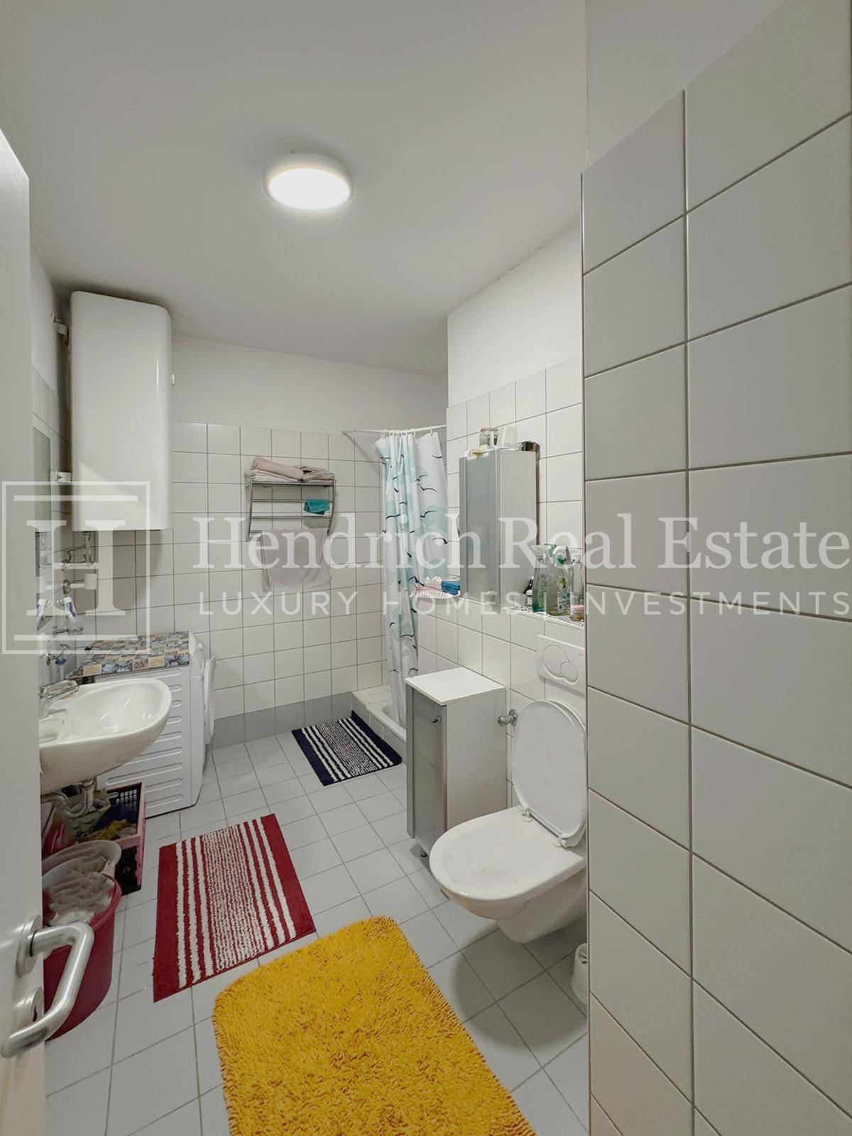 Helles Badezimmer mit weißen Fliesen, Dusche, WC und Waschbecken.
