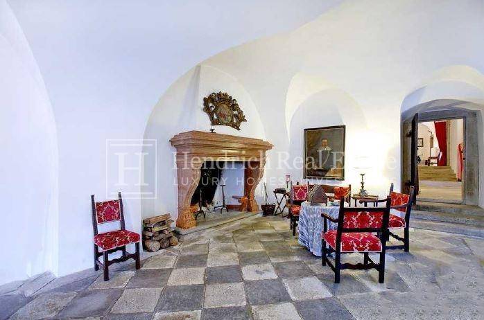 Historischer Raum mit Gewölbedecke, Steinfliesenboden und einem imposanten Kamin, eingerichtet mit antiken Möbeln.