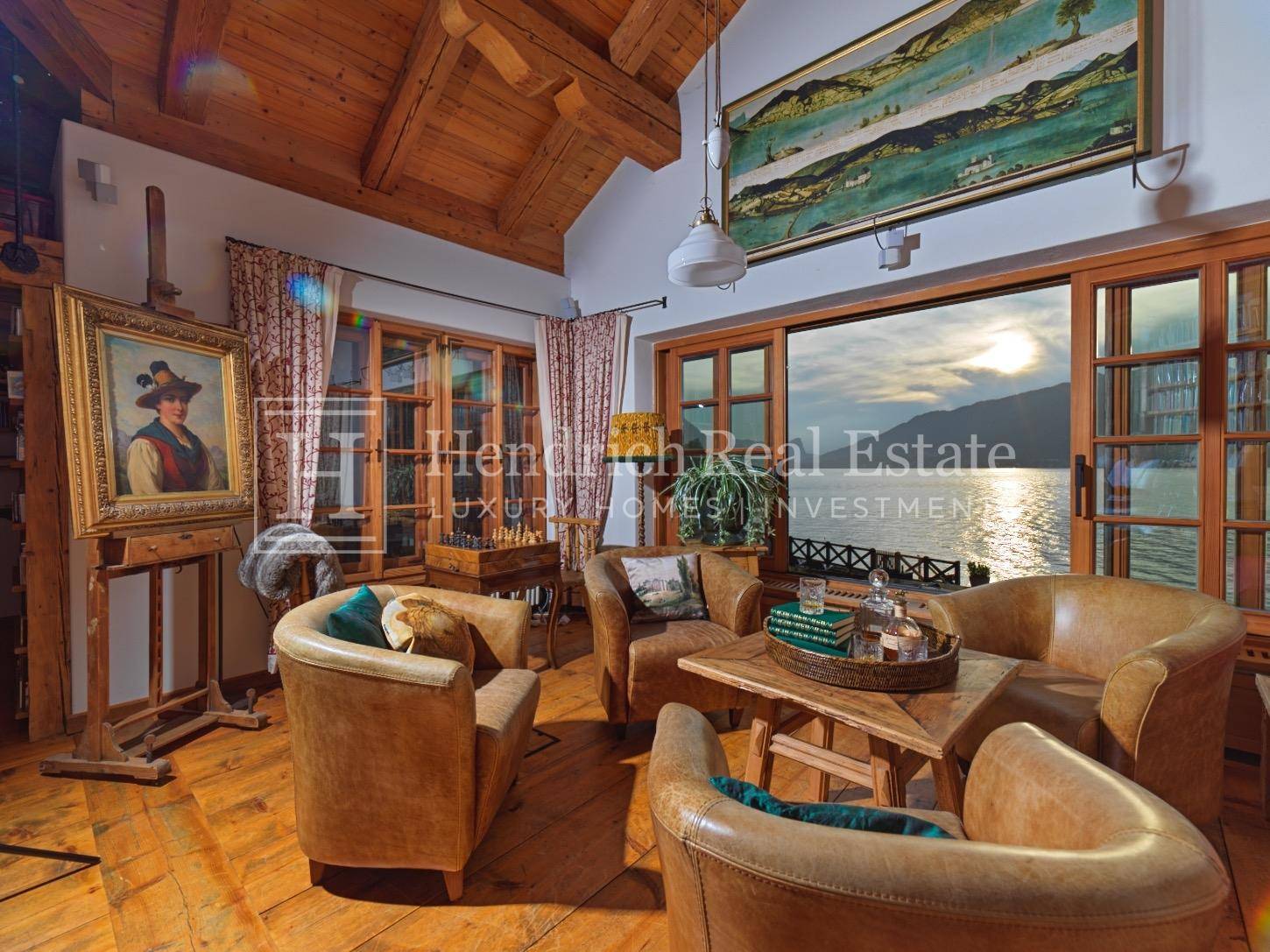 Rustikales Wohnzimmer mit Ledersesseln, Holzbalkendecke und Panoramablick auf den See.