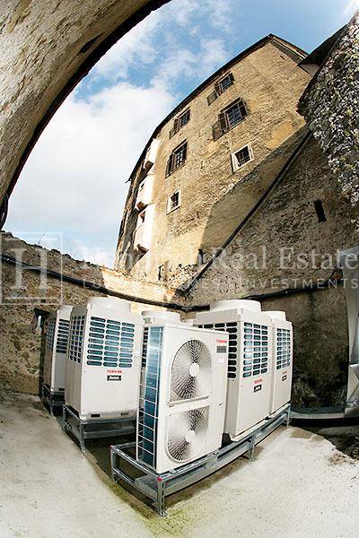 Mehrere Klimaanlagen-Außengeräte unter einem Steinbogen vor dem historischen Schlossgebäude.