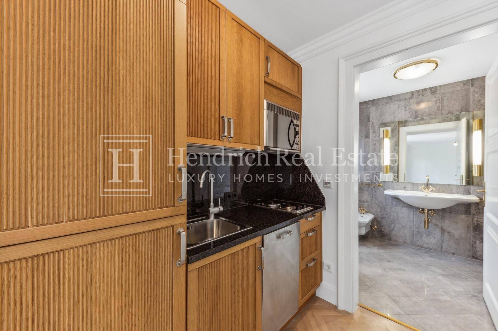Kompakte Küchenzeile mit Holzfronten, Granitarbeitsplatte und Blick auf ein angrenzendes Badezimmer.