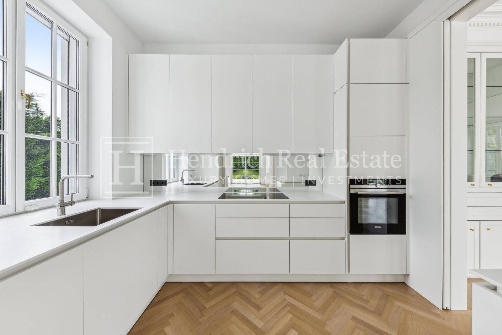 Moderne weiße Einbauküche mit minimalistischem Design, integrierten Geräten und Fensterblick ins Grüne.