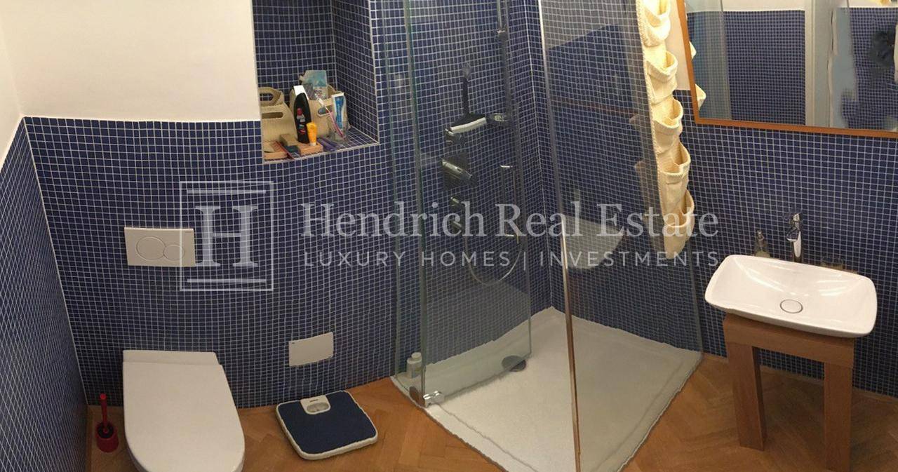 Badezimmer mit blauen Mosaikfliesen, moderner Duschkabine und wandhängendem WC.