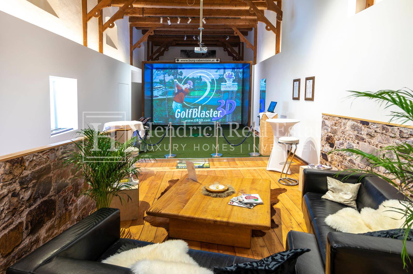 Freizeitraum mit Golfsimulator, bequemen Ledersofas und rustikalem Holztisch unter Deckenbalken.