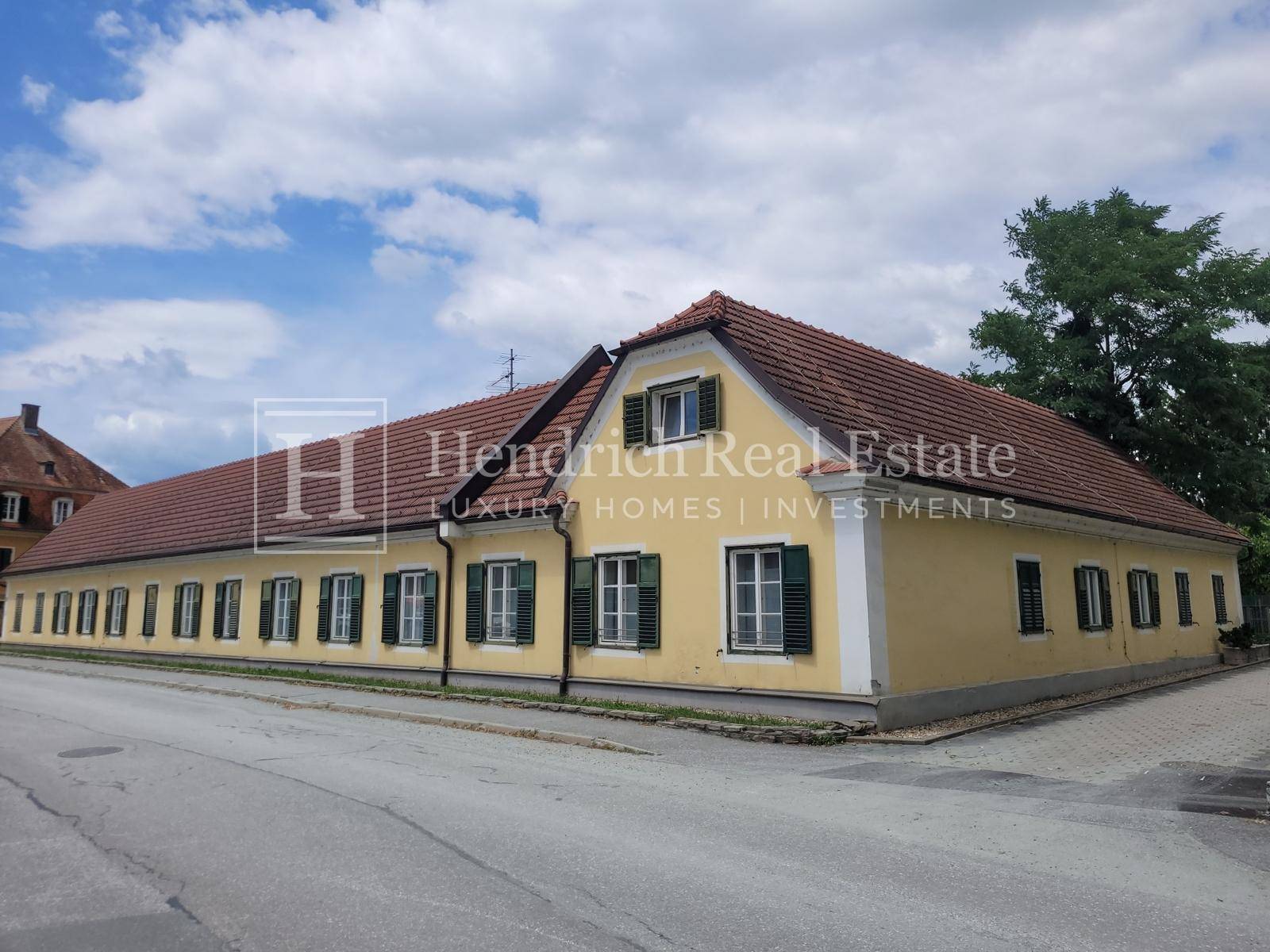 Langes, historisches Gebäude mit gelber Fassade, roten Dachziegeln und vielen Fenstern zur Straße.