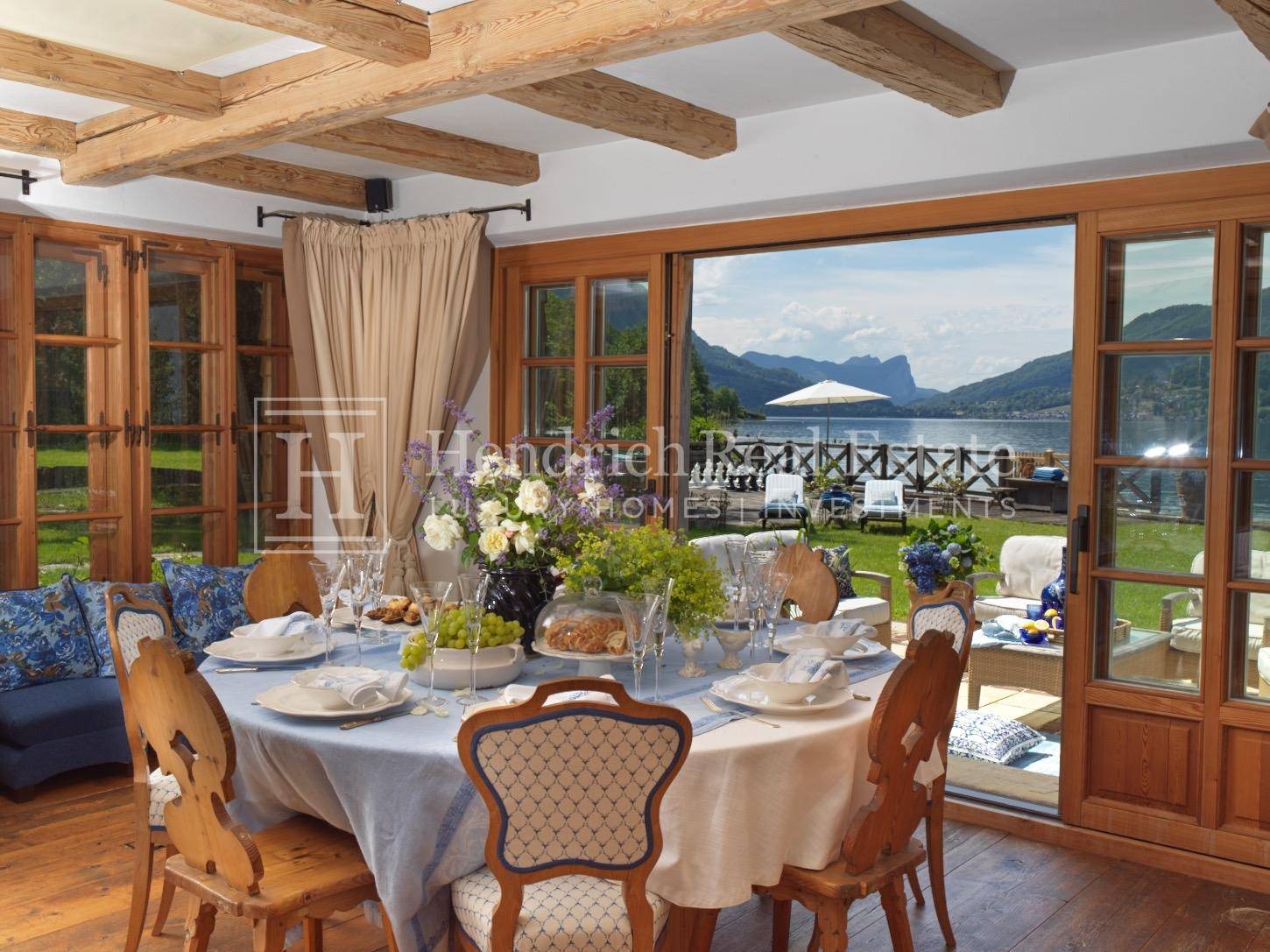 Eleganter Essbereich mit Holzbalkendecke und großen Fenstern mit Seeblick.