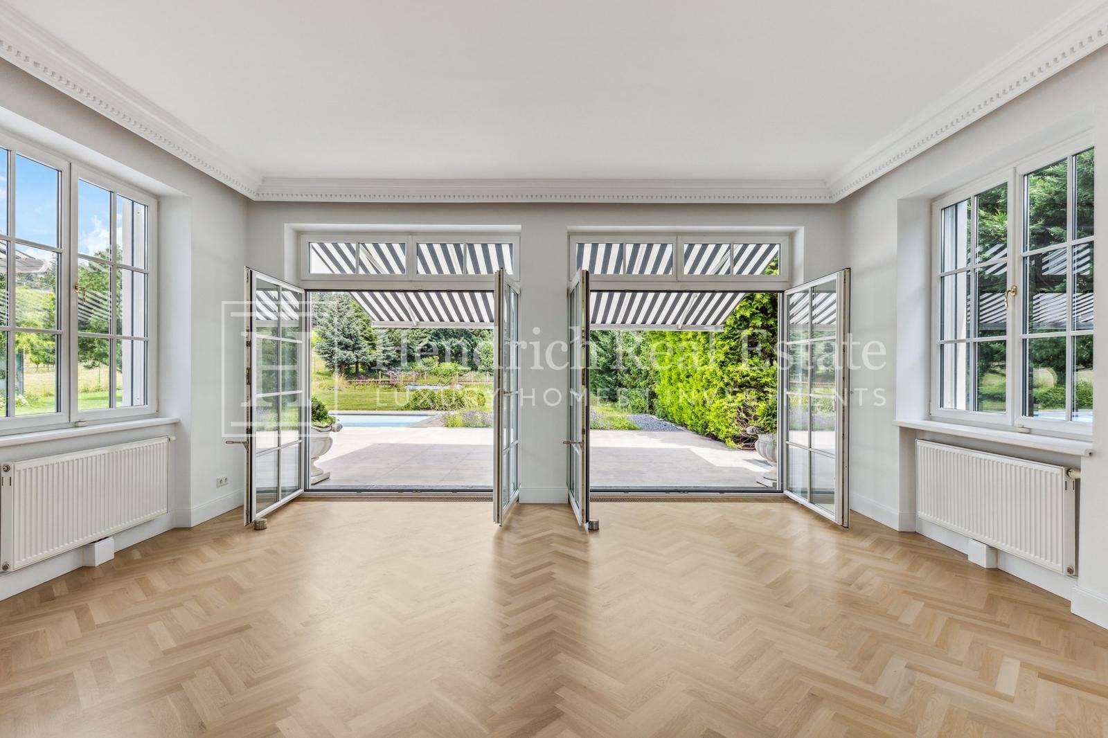 Helles Wohnzimmer mit elegantem Fischgrätparkett und direktem Zugang zur Terrasse und zum Garten.